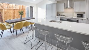 A modern kitchen with white cabinets, a large island, and a dining area with yellow chairs. - Host Stay Littlebeck House Briggswath (Whitby)