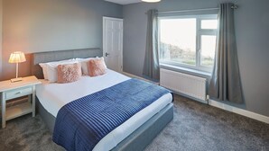 Un dormitorio con cama, mesita de noche, lámpara, ventana con cortinas y radiador.