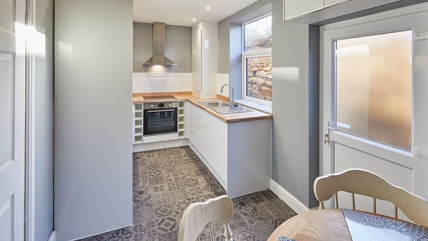 Una cocina compacta con horno integrado, ventana con vista a una pared de piedra y piso con diseño.