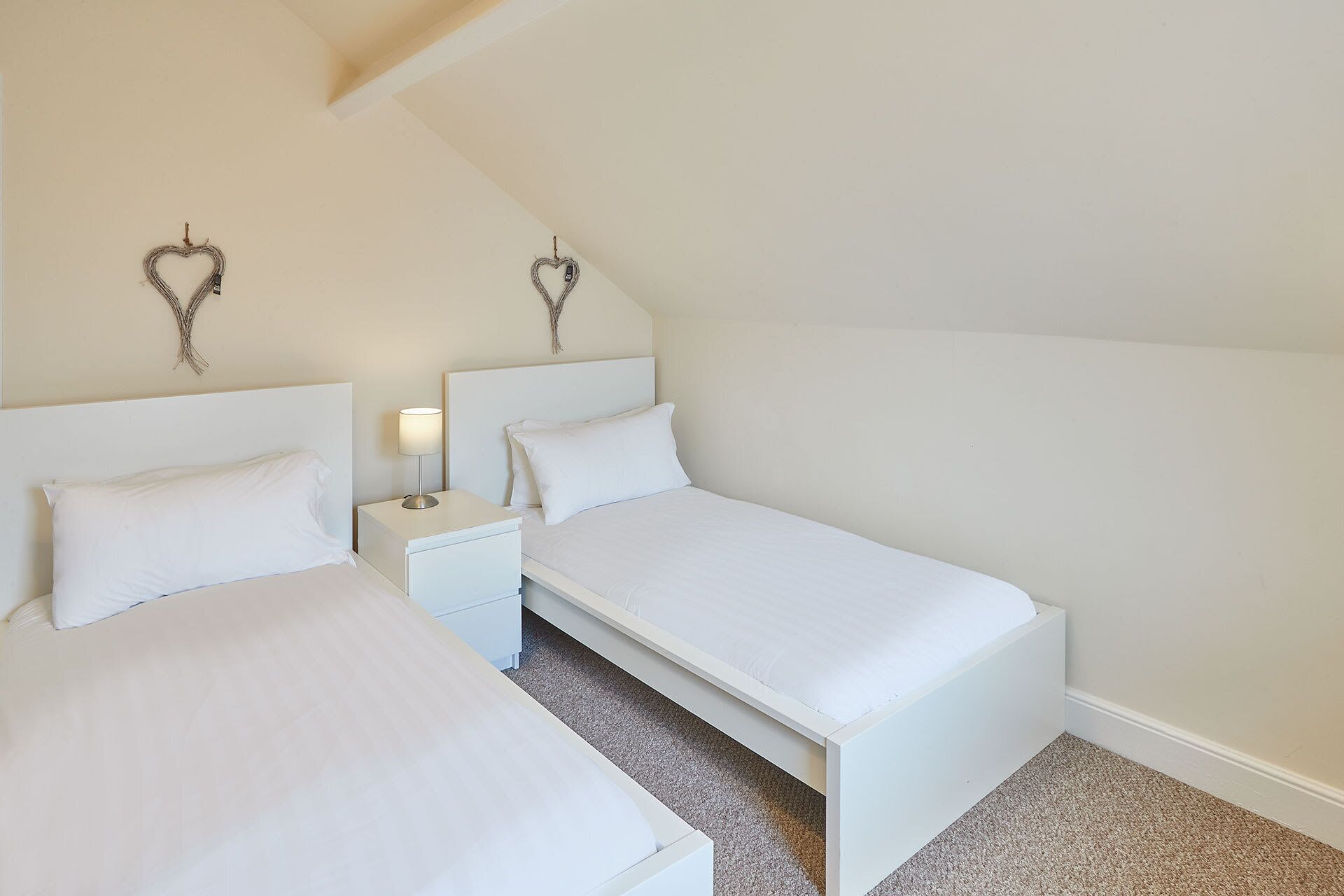 A bedroom with two single beds, a nightstand with a lamp, and decorative wall art.