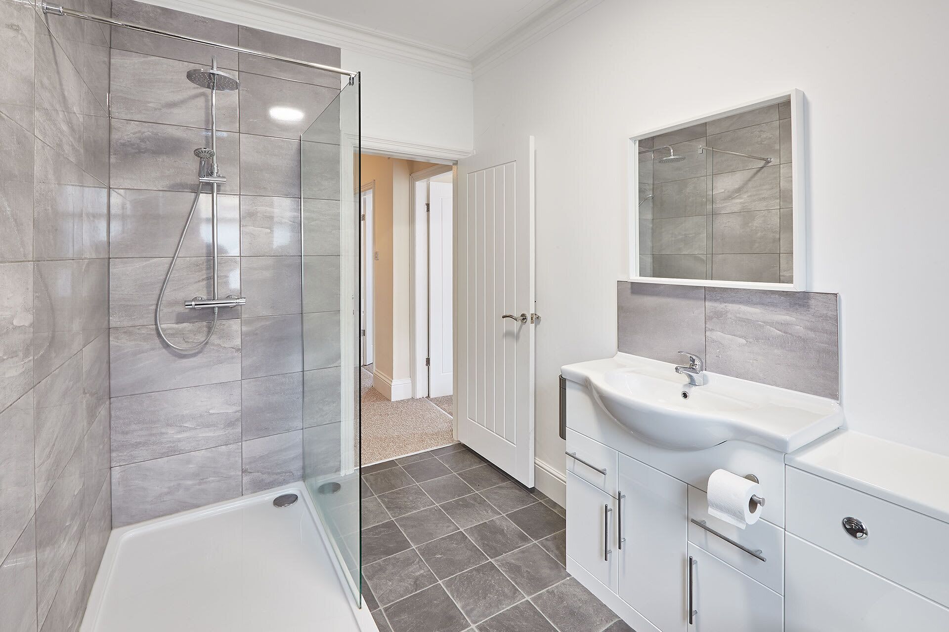 Een moderne badkamer met een douchecabine van glas, een wit wastafelmeubel en een spiegel erboven.