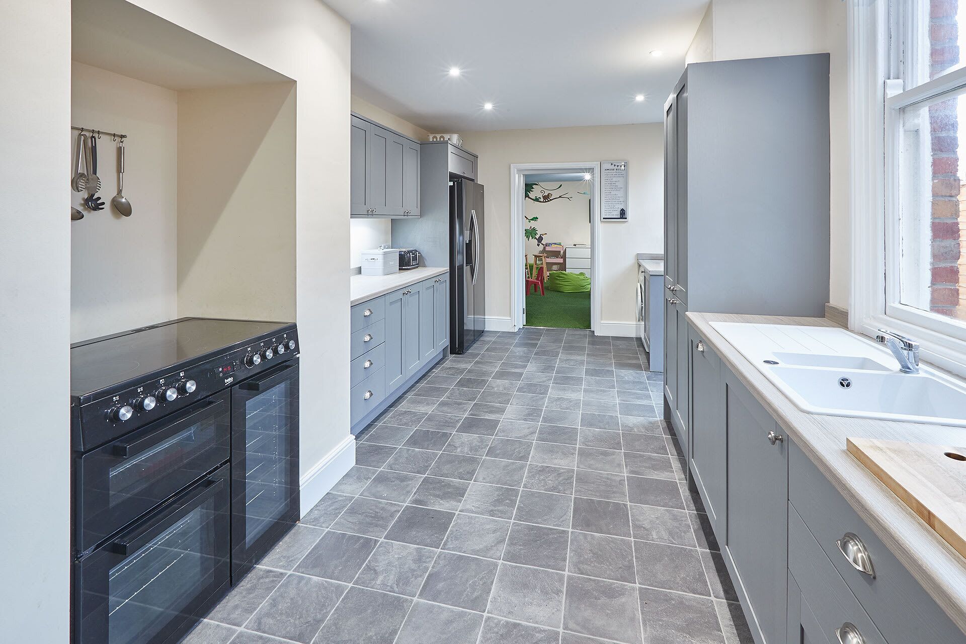 A modern kitchen with grey cabinets, a black oven, and a large window.