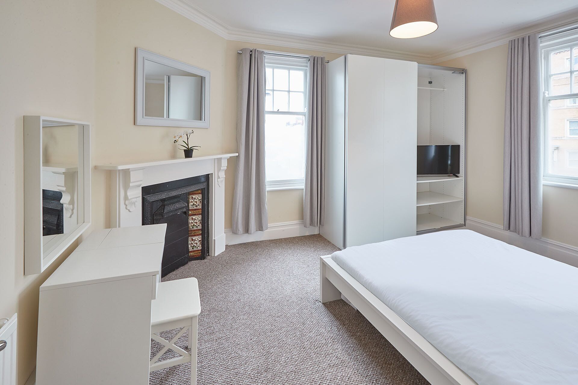 A bedroom with a bed, a dresser, a mirror, a fireplace, and a television on a shelf.