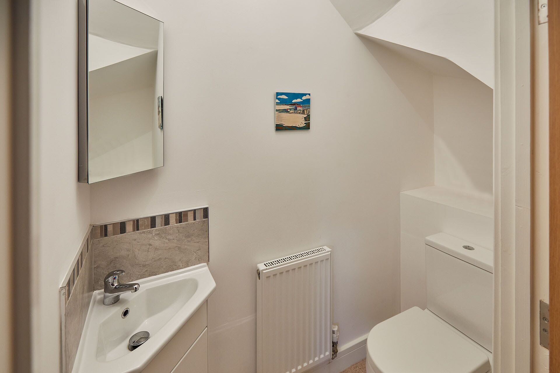 Une salle de bain avec un lavabo, un miroir, un radiateur, des toilettes et un petit tableau accroché au mur.