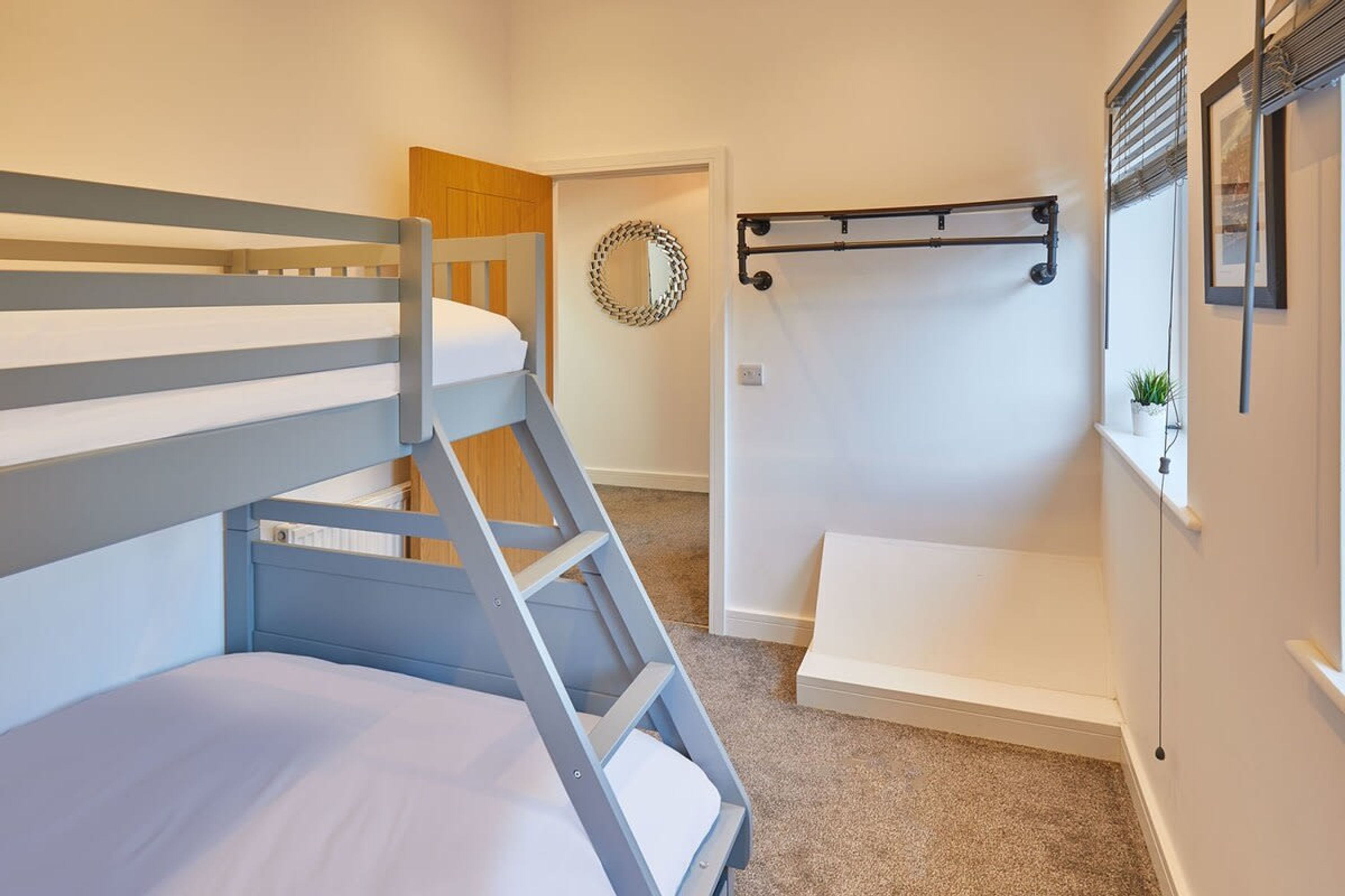 Une chambre avec un lit superposé, une échelle, un petit banc, un miroir et une plante posée sur une étagère.