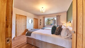 A bedroom with two beds, wooden doors, a chandelier, and a window with a view of trees. - Host Stay The Parlour (Newcastle-upon-Tyne)