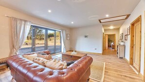 A spacious living room with a leather sofa, a coffee table, and large windows offering a view of the outdoors. - Host Stay The Parlour (Newcastle-upon-Tyne)