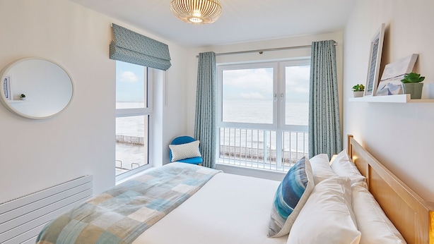 A bedroom with a large bed, a round mirror, and a view of the sea through the windows.