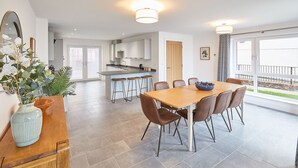 A modern kitchen with a central island, a dining area with a wooden table and chairs, and a large window offering a view of the outdoors.