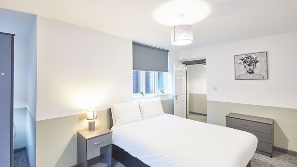Um quarto moderno com uma cama grande, uma mesa de cabeceira com abajur, cômoda e uma janela com persianas.