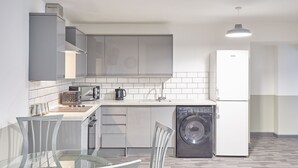 Cozinha moderna com armários cinza, lava-louças, máquina de lavar roupa e mesa de jantar de vidro com cadeiras.