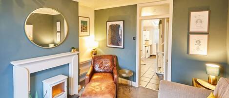 Un salon avec une cheminée, un fauteuil en cuir, un canapé et un grand miroir rond accroché au mur.