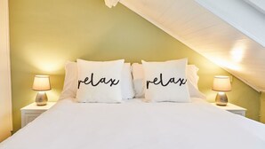 A bedroom with a bed, two bedside lamps, and pillows with the word "relax" on them. - Host Stay Harbour Mist Cottage (Whitby)