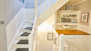 A staircase leading to a kitchen area with white cabinetry and a wooden countertop. - Host Stay Harbour Mist Cottage (Whitby)