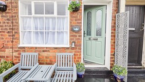 A brick house with a green door, white window with curtains, and a small garden table with chairs. - Host Stay Harbour Mist Cottage (Whitby)