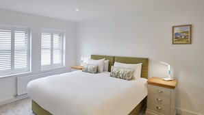 A bedroom with a large bed, two bedside tables, and a window with blinds. - Host Stay Even Keel (Whitby)