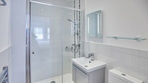 A modern bathroom with a glass shower enclosure, a white sink, and a toilet. - Host Stay Even Keel (Whitby)