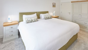A neatly arranged bedroom with a large bed, bedside tables, a wardrobe, and a small bedside lamp. - Host Stay Even Keel (Whitby)