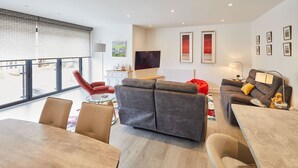 A modern living room with a sofa, chairs, a TV, and artwork on the walls. - Host Stay Even Keel (Whitby)