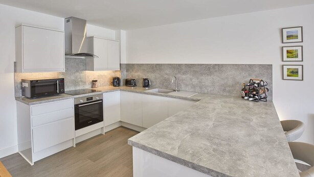 A modern kitchen with white cabinetry, a built-in oven, a microwave, a coffee maker, and a sink. - Host Stay Even Keel (Whitby)
