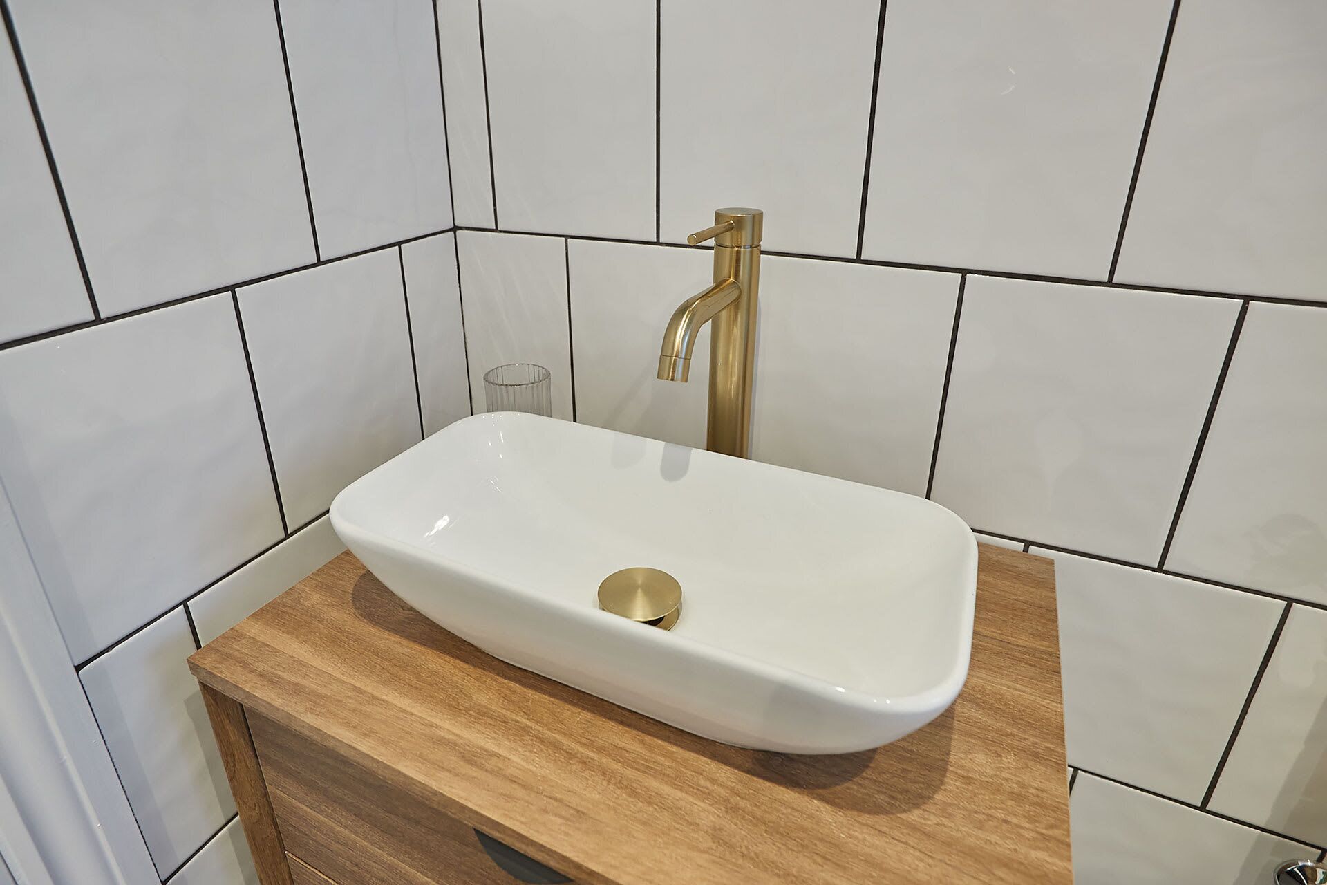 Ein Badezimmer mit einem weißen Waschbecken, einem goldfarbenen Wasserhahn und einer Holzauslage.
