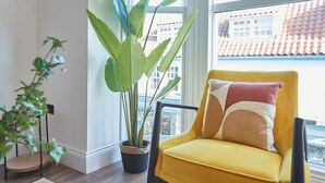 A yellow armchair with a patterned cushion, a large potted plant, and a view of buildings through a window. - Host Stay Abbey Nook (Whitby)