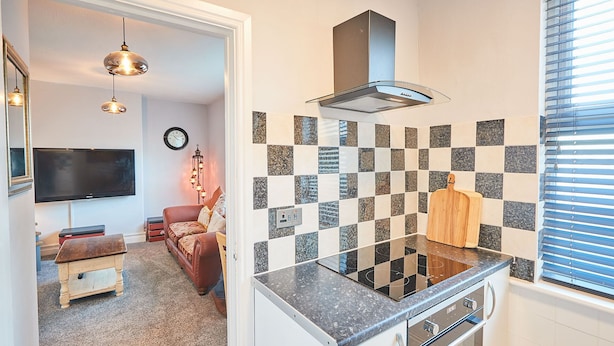 A modern kitchen with a black and white checkered backsplash, a built-in stove, and a wooden cutting board. - Host Stay Seas The Day (Saltburn-by-the-Sea)
