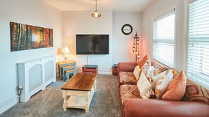 A living room with a wooden coffee table, a sofa with patterned cushions, a flat-screen TV, a painting on the wall, a lamp, and a clock. - Host Stay Seas The Day (Saltburn-by-the-Sea)