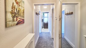 A hallway with a painting of flowers, a mirror, and a door leading to a bathroom. - Host Stay Seas The Day (Saltburn-by-the-Sea)