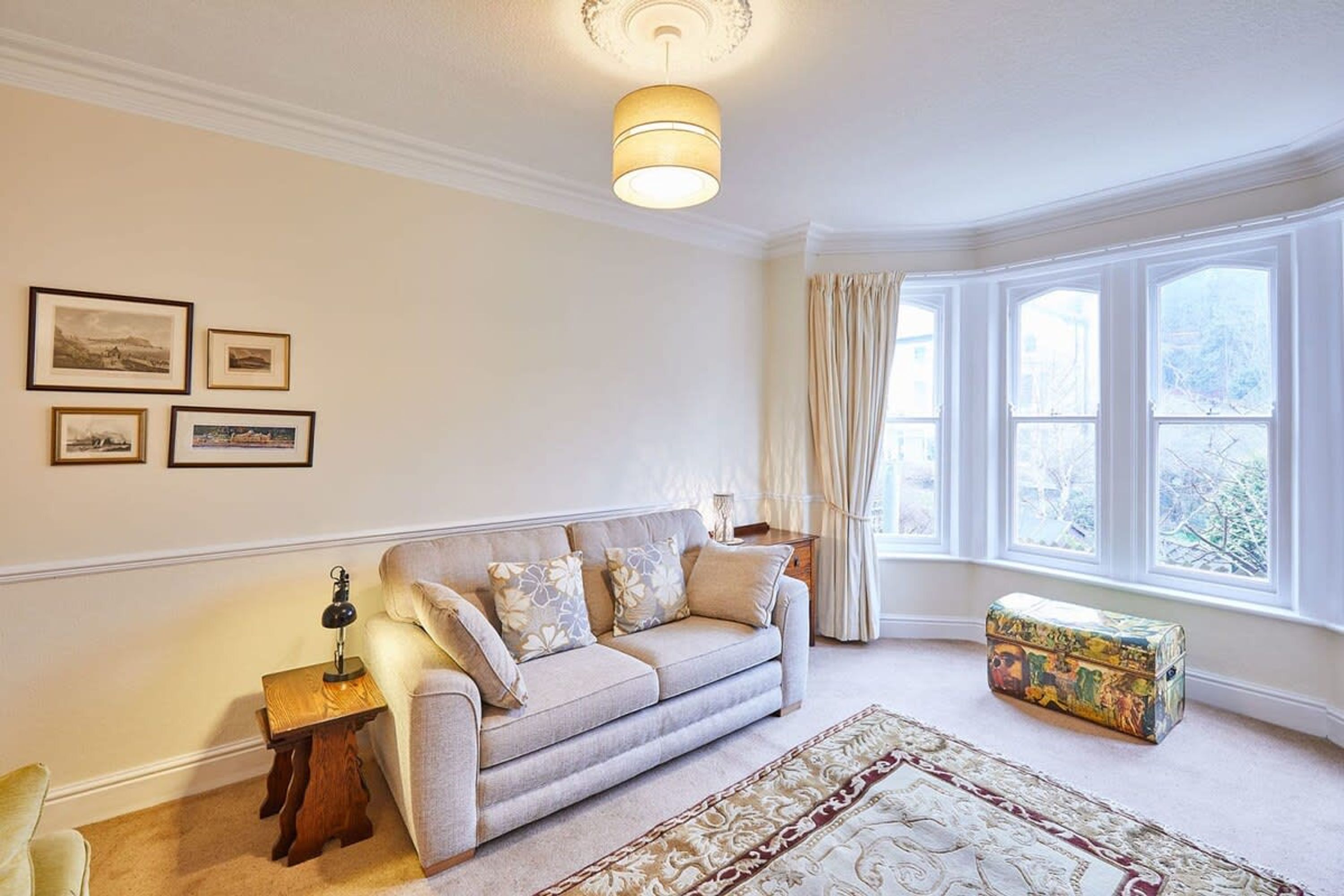 A living room with a beige sofa, a patterned rug, and a window with curtains.