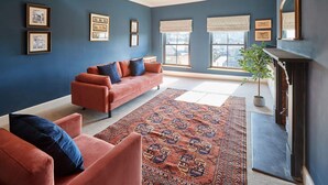 A living room with a blue wall, a red sofa, a patterned rug, and a fireplace. - Host Stay Turnstone (Saltburn-by-the-Sea)