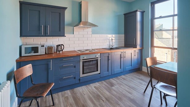A modern kitchen with blue cabinets, a wooden countertop, and a view through a large window. - Host Stay Turnstone (Saltburn-by-the-Sea)
