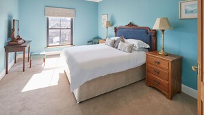 A bedroom with a large bed, a wooden nightstand, a chair, a window with a view, and a chandelier. - Host Stay Turnstone (Saltburn-by-the-Sea)