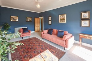 Un salon avec un mur bleu, un canapé rose, un tapis à motifs rouges et des tableaux encadrés accrochés au mur.