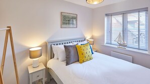 A bedroom with a bed, bedside lamps, a window with blinds, a ship model, and a framed picture on the wall. - Host Stay Jet Cottage Spa Well (Whitby)