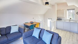 A modern apartment with a loft-style living area, a dining table, and a kitchen with a window. - Host Stay Jet Cottage Spa Well (Whitby)