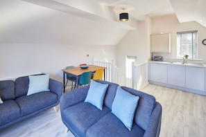 Eine moderne Wohnung mit einem Loft-Wohnbereich, einem Esstisch und einer Küche mit Fenster.