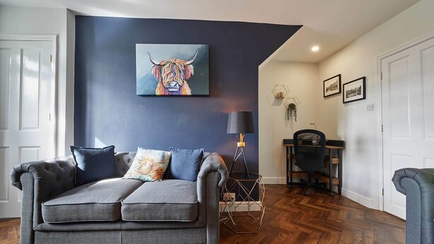A living room with a grey sofa, a painting of a bull, and a lamp. - Host Stay Cummins Goings Cottage (Barnard Castle)