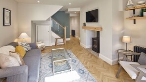 A modern living room with a grey sofa, a coffee table, and a fireplace. There is a staircase leading to another level. - Host Stay The Salt Nook (Whitby)