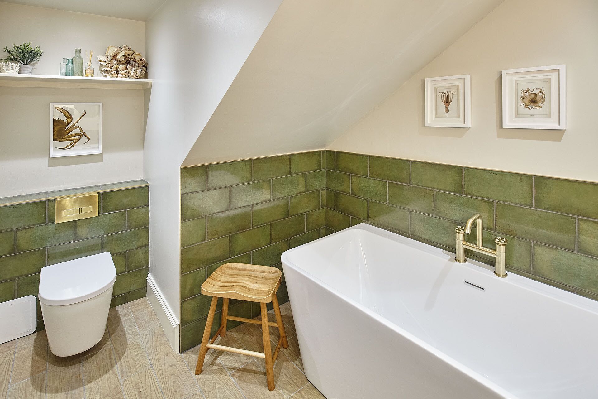 A bathroom with a white bathtub, green tiled walls, a wooden stool, and a toilet.