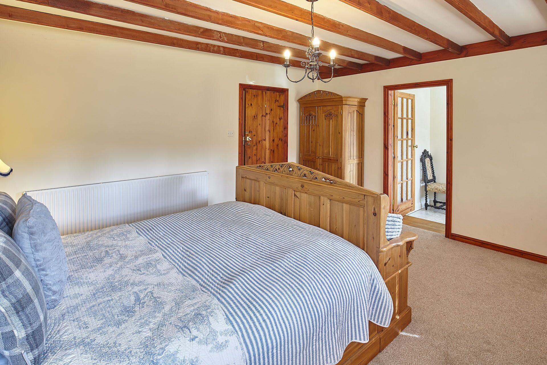 A bedroom with a wooden bed, a radiator, a chandelier, and wooden wardrobes.