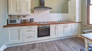 A kitchen with white cabinets, a microwave, a stove, and an oven. - Host Stay Sandpiper (Saltburn-by-the-Sea)