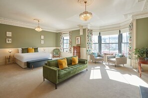 A spacious hotel room with a large bed, a green sofa, and a view of the city through large windows. - Host Stay Sandpiper (Saltburn-by-the-Sea)