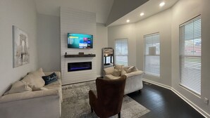 Un salon moderne avec un téléviseur à écran plat fixé à un mur blanc, deux canapés, un fauteuil marron et une cheminée.