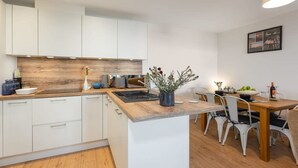 Uma cozinha moderna com armários brancos, bancada de madeira e um espaço de refeições com mesa e cadeiras.