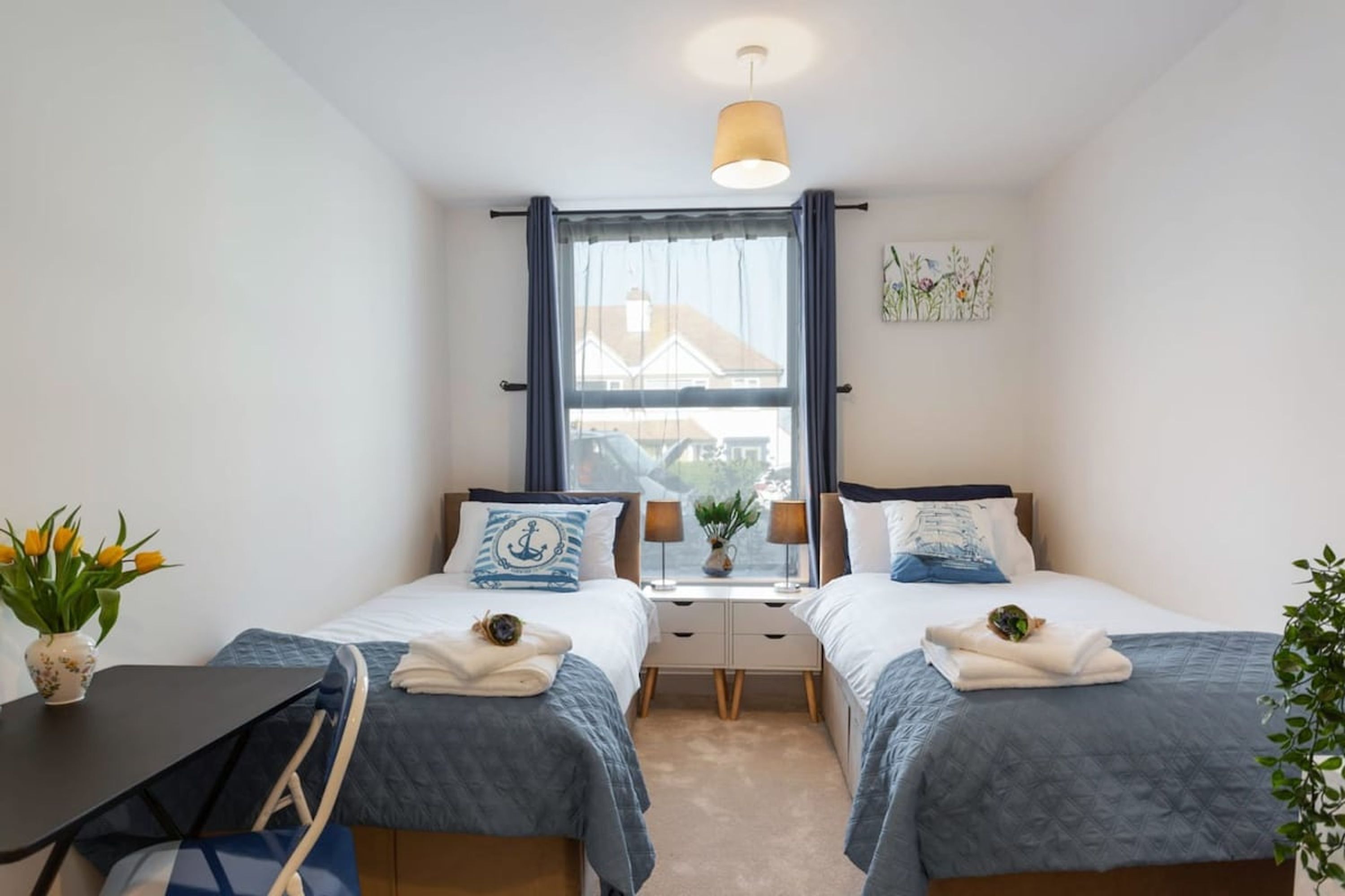 A bedroom with two beds, a small table, and a window with curtains.