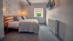 Ein Schlafzimmer mit einem Bett, einem Nachttisch, einem Fenster, einer Heizung und einem an der Wand befestigten Fernseher.