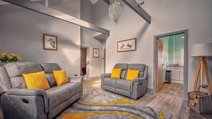 Ein modernes Wohnzimmer mit grauen Sofas, gelben Kissen, einer Chandelierleuchtre, gerahmten Kunstwerken und einem Holzboden.