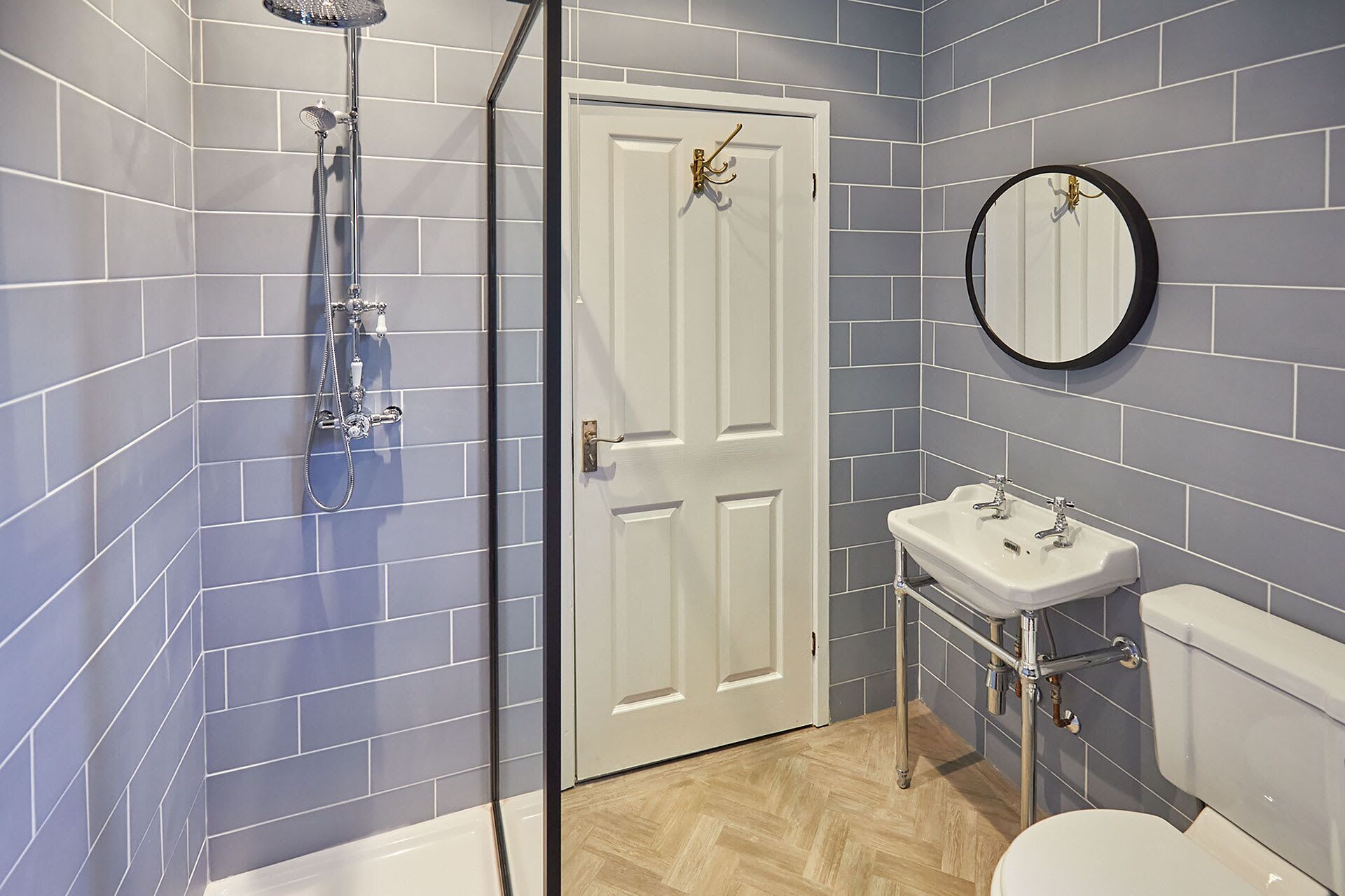 A bathroom with a shower, sink, toilet, and a door with a towel rack.