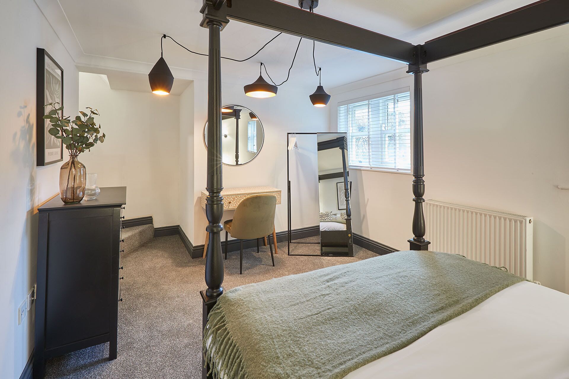 Un lit à baldaquin avec un couvre-lit vert, un bureau avec une chaise, un miroir et un radiateur.